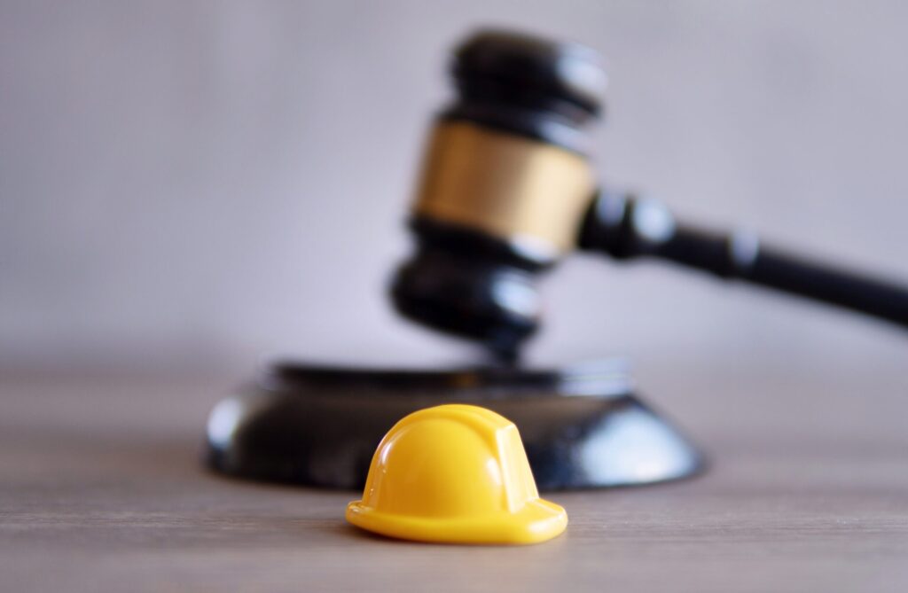 Judge's gavel blurred in the background with a miniature yellow hardhat in the foreground